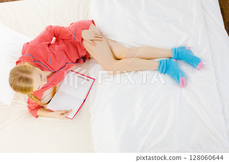 Woman relaxing in bed reading book 128060644