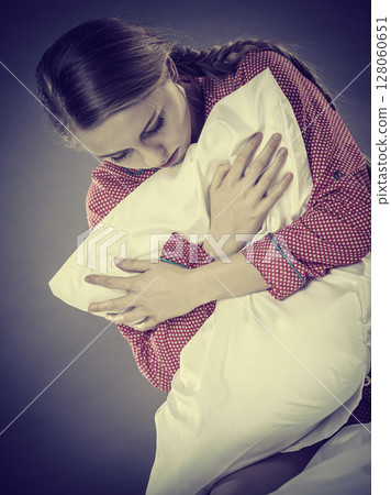 Sad depressed girl in bed gripping pillow 128060651