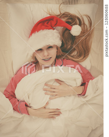 Happy woman wearing pajamas and Santa Claus hat 128060688