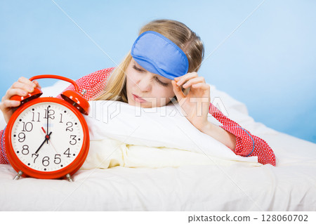 Sleeping woman wearing pajamas holding clock 128060702