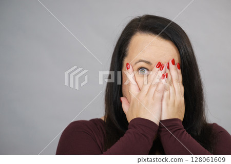 Woman peeking through her hands Woman peeking through her hands 128061609