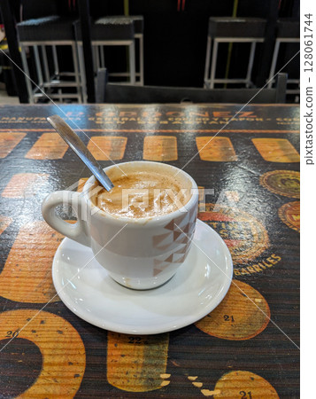 A cup of coffee sits on a patterned table, ready for a relaxing coffee break in a cafe or restaurant setting. A cup of coffee sits on a patterned table, ready for a relaxing coffee break in a cafe or restaurant setting. 128061744