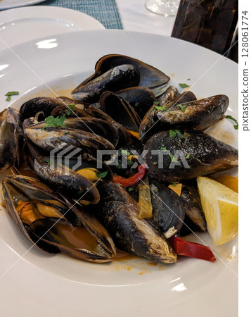 Delicious plate of mussels, served with fresh herbs, lemon, and bell peppers. This seafood dish is ready to be enjoyed at the restaurant. Delicious plate of mussels, served with fresh herbs, lemon, and bell peppers. This seafood dish is ready to be enjoyed at the restaurant. 128061774