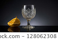 Crystal glass and a slice of citrus fruit standing on a reflective surface 128062308