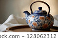 Decorated ceramic teapot with wooden handle standing on wooden tray 128062312