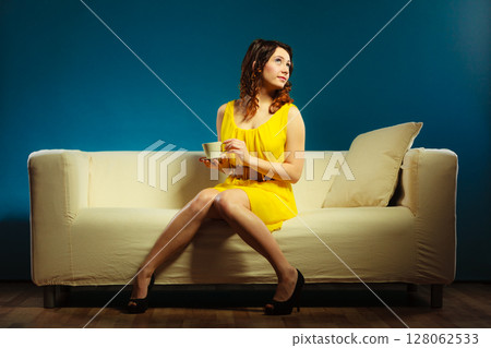 woman sitting on sofa holds coffee cup 128062533