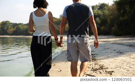 Romantic couple holding hands of each other and walking at coastline. Happy pair going along seashore at sunny day. Lovers spending time together at resort. Concept of vacation or holiday. Slow motion Romantic couple holding hands of each other and walking at coastline. Happy pair going along seashore at sunny day. Lovers spending time together at resort. Concept of vacation or holiday. Slow motion 128063501