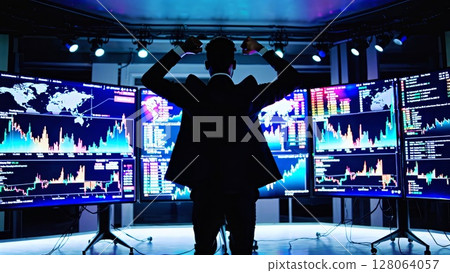 Successful stock trader is raising arms in a dark room full of monitors showing real time data, graphs, and maps celebrating his latest trade 128064057