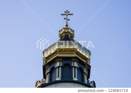 Historic church dome featuring intricate designs and a prominent cross shines brightly in the morning light against a blue sky Historic church dome featuring intricate designs and a prominent cross shines brightly in the morning light against a blue sky 128065719