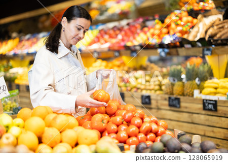 Middle-aged woman choosing tomatoes in grocery store 128065919
