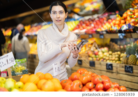 Female looking at shop windows in greengrocery with phone Female looking at shop windows in greengrocery with phone 128065939