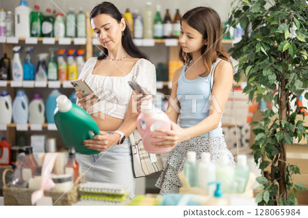 Woman with teen daughter buyer scans qr code on liquid laundry powder label 128065984