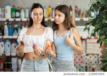 Uncertain mother and daughter choosing nail polish in supermarket 128065994