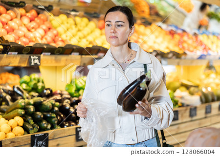 Middle-aged woman holding eggplants in grocery store Middle-aged woman holding eggplants in grocery store 128066004