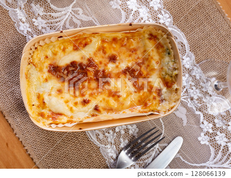 On wooden table Italian dish is lasagna baked in oven under cheese crust On wooden table Italian dish is lasagna baked in oven under cheese crust 128066139
