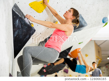 Woman grabbing ledges of artificial climbing wall Woman grabbing ledges of artificial climbing wall 128066165