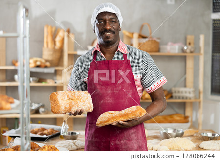 Portrait of experienced baker with tasty hot bread and baguettes in hands in kitchen Portrait of experienced baker with tasty hot bread and baguettes in hands in kitchen 128066244
