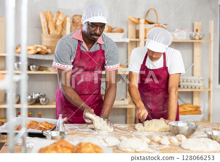 Two skilled bakers kneading and slicing dough in cozy bakery 128066253