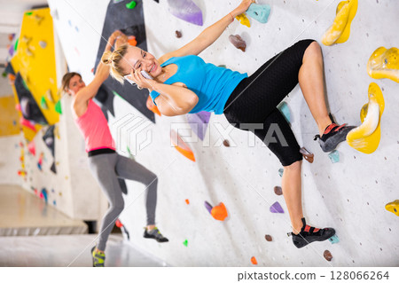 Woman talking on phone while exercising in climbing gym Woman talking on phone while exercising in climbing gym 128066264