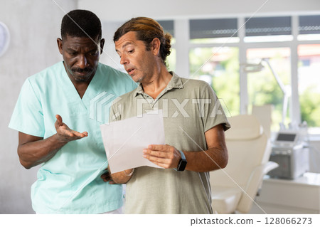 African American aesthetician and male patient discussing bill for cosmetic services African American aesthetician and male patient discussing bill for cosmetic services 128066273