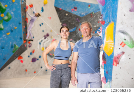 Sporty young girl and aged man standing near bouldering wall 128066286