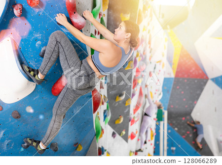 Young female alpinist practicing indoor rock-climbing on artificial boulder without safety belts Young female alpinist practicing indoor rock-climbing on artificial boulder without safety belts 128066289