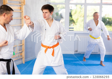 Young guy and his coach practice punches in karate sparring in gym Young guy and his coach practice punches in karate sparring in gym 128066293