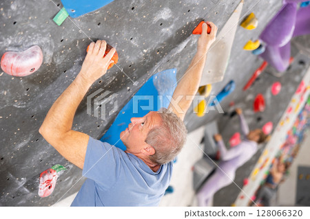 Male mountaineer climbing artificial rock wall without belay indoors Male mountaineer climbing artificial rock wall without belay indoors 128066320
