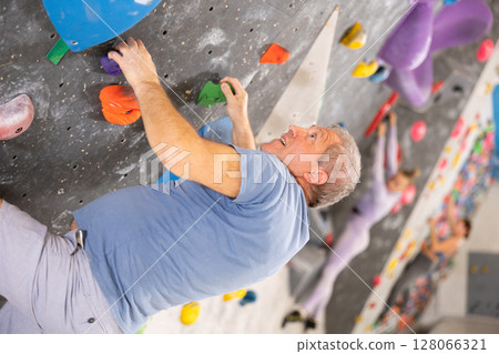 Older man climbing without ropes and harnesses on bouldering wall 128066321