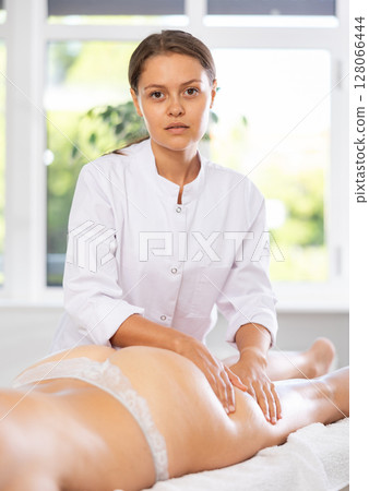 Young female masseur doing glutes and hamstring massage to woman client Young female masseur doing glutes and hamstring massage to woman client 128066444