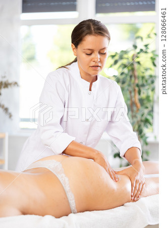 Professional young female therapist doing thigh and buttocks massage to woman 128066461