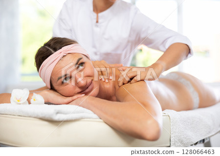 Young woman enjoying back and shoulders massage from professional masseuse Young woman enjoying back and shoulders massage from professional masseuse 128066463