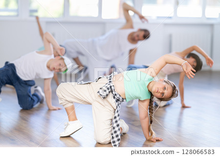 Cheerful sports preteen girls and boys hip hop dancers doing dance workout on floor with male trainer during group class 128066583