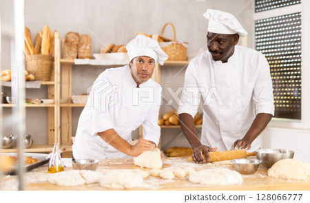 African man and male assistant make dough, employee kneads dough, assistant works with rolling pin 128066777