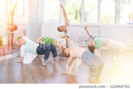 Dynamic young girl sitting in breakdance pose in dance studio with other teenage dancers 128066782