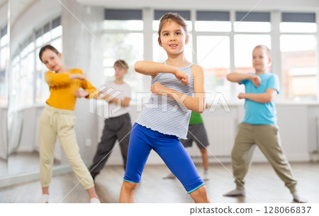 Positive juvenile girl engaged in breakdancing in training room with children's group 128066837