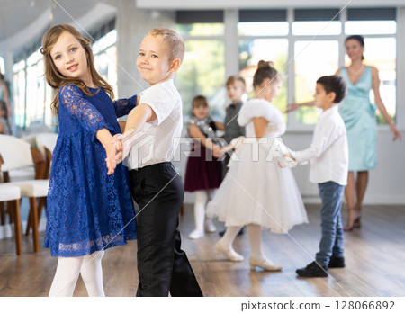 Little children in elegant dresses practicing waltz dance in school hall 128066892