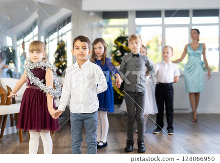 Little children in elegant dresses standing in pairs in dance pose in school hall Little children in elegant dresses standing in pairs in dance pose in school hall 128066950