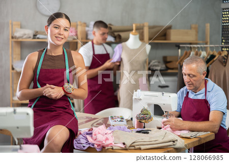 Female model sitting on a table in front of male tailors 128066985