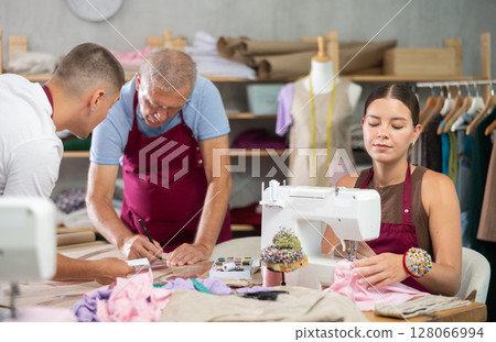 Male tailors drawing a sketch together next to a seamstress 128066994