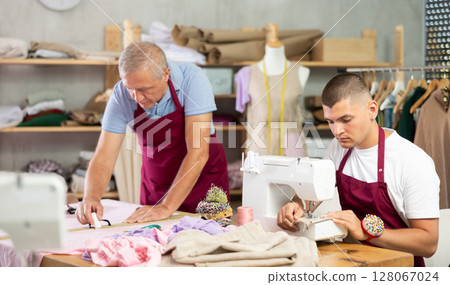Young guy sews on machine male assistant drawing pattern 128067024