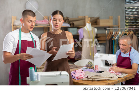 Female dressmaker with assistant reading documents in front of tailor 128067041