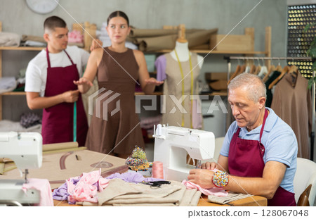 Tailor takes measurements from a woman next to an elderly employee of the atelier 128067048