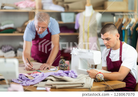 young tailor sews next to a mature employee of the atelier 128067070