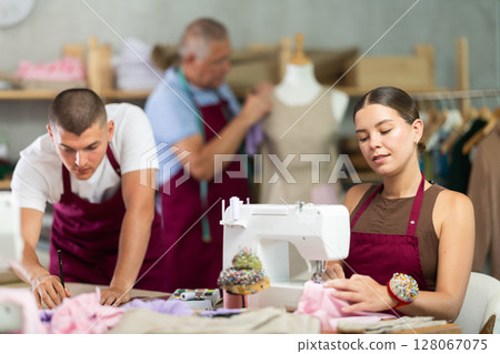 Female seamstress working on a typewriter next to a team of tailors Female seamstress working on a typewriter next to a team of tailors 128067075