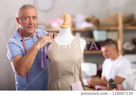 Elderly man working with mannequin, young man sewing 128067130