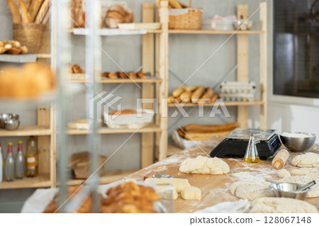 Professional bakery kitchen with work table, bread bun baking in deck, stuff, dough, cabinet and ingredient for baking. Close up 128067148