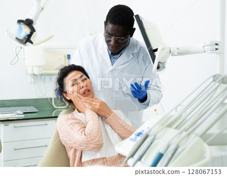 Woman patient who came to an appointment with a male dentist is sitting in a dental chair in clinic office, showing which side of her tooth aches 128067153