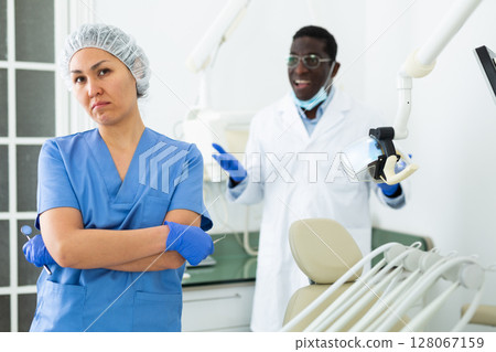 Frustrated female dental assistant standing in office with disgruntled doctor 128067159