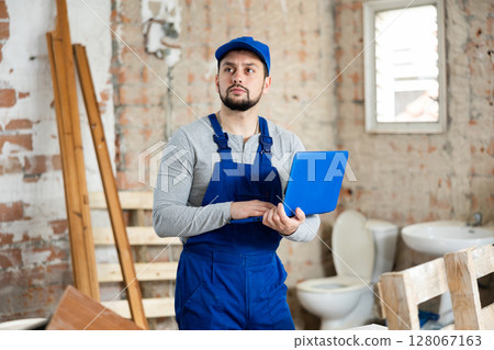 Builder handyman checking plan of house renovation on laptop 128067163